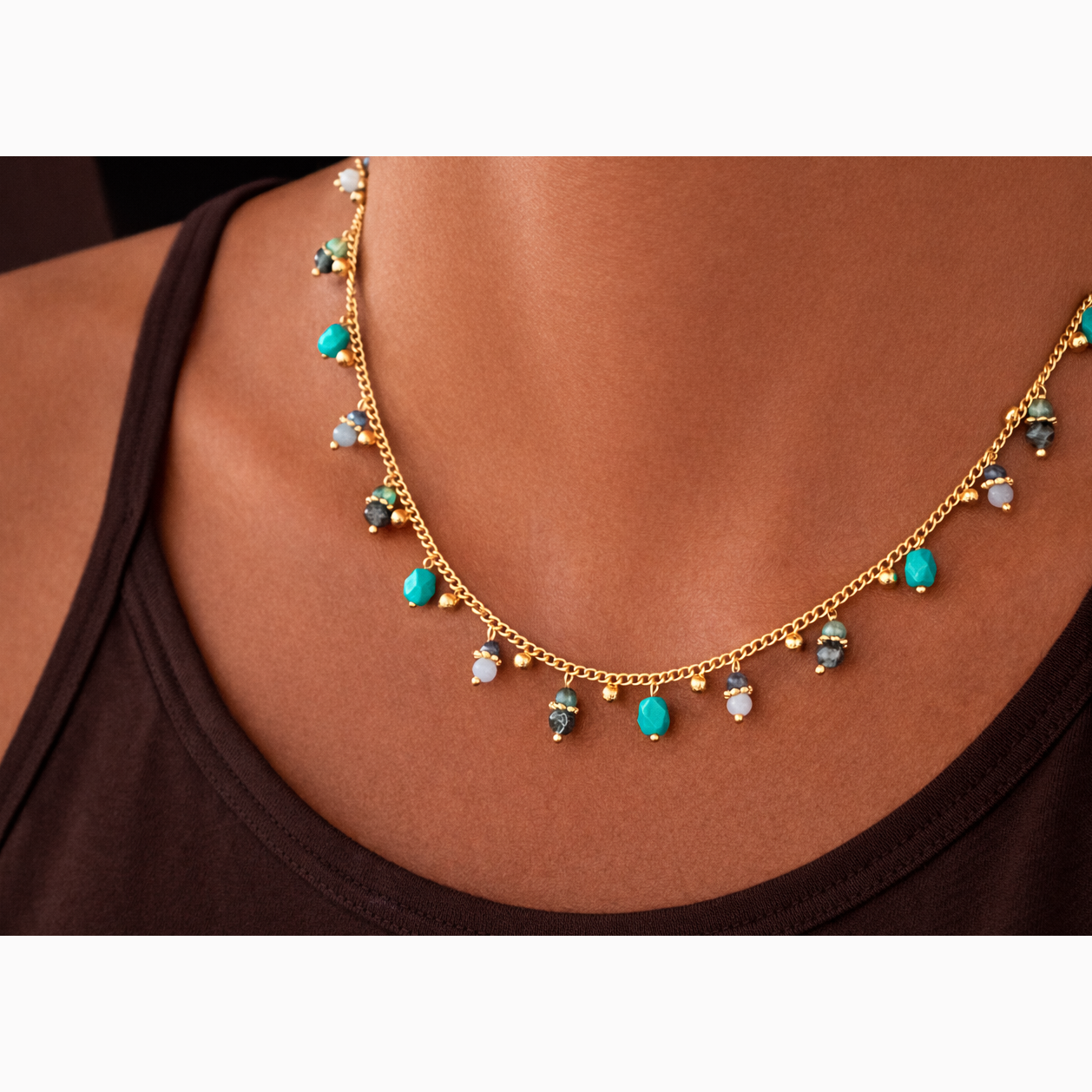 Gold necklace with turquoise gemstones on a person wearing a black top.