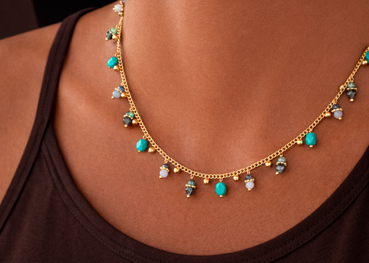 Gold necklace with turquoise and clear gemstones on a person wearing a black top.
