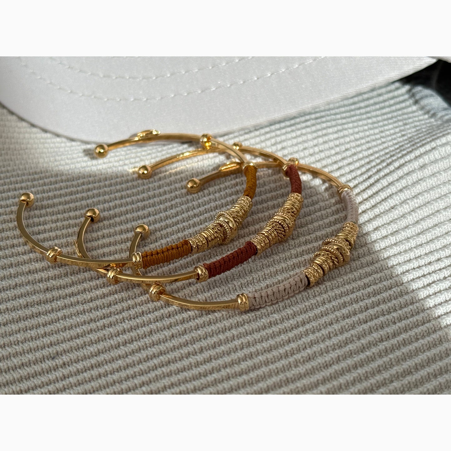 Gold and brown threaded bracelets on a textured surface