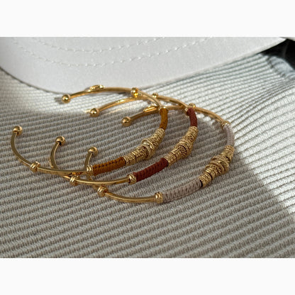 Gold and brown threaded bracelets on a textured surface
