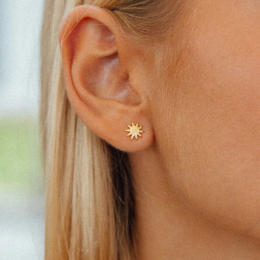 sun burst gold studs close up on womans ear