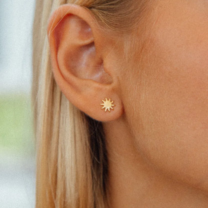 sun burst gold studs close up on womans ear