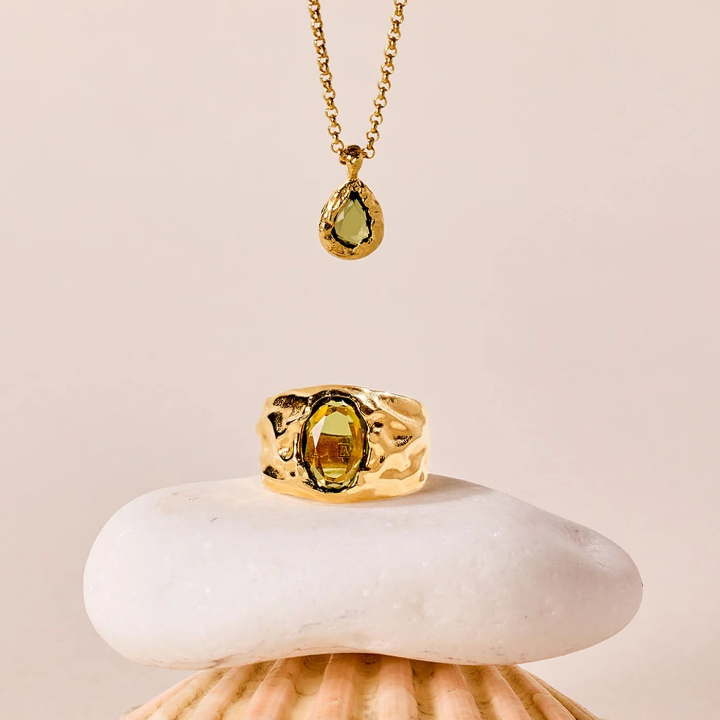 Gold ring and necklace with a green gemstone on a shell against a beige background