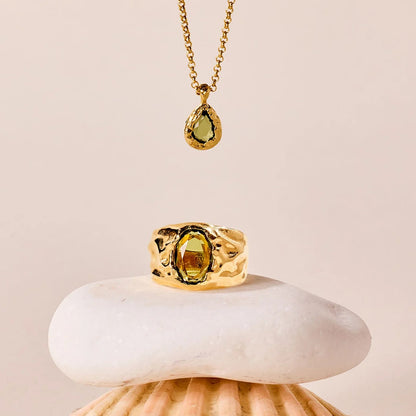 Gold ring and necklace with a green gemstone on a shell against a beige background