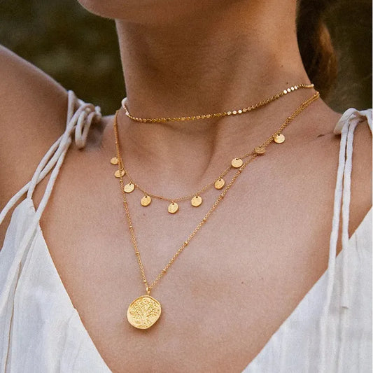 Gold necklaces on a person wearing a white top with a blurred natural background