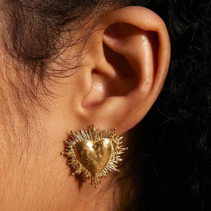 Close-up of an ear wearing a gold heart-shaped earring with a textured design.