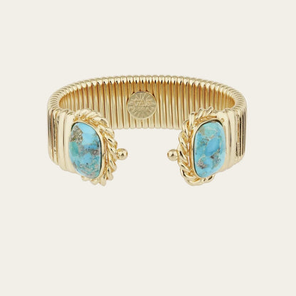 A gold-toned metal cuff bracelet featuring two oval turquoise-blue stone inlays on the front, set against a plain white background.