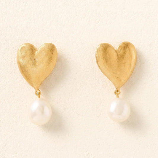 Gold heart-shaped earrings with pearl drops on a light beige background