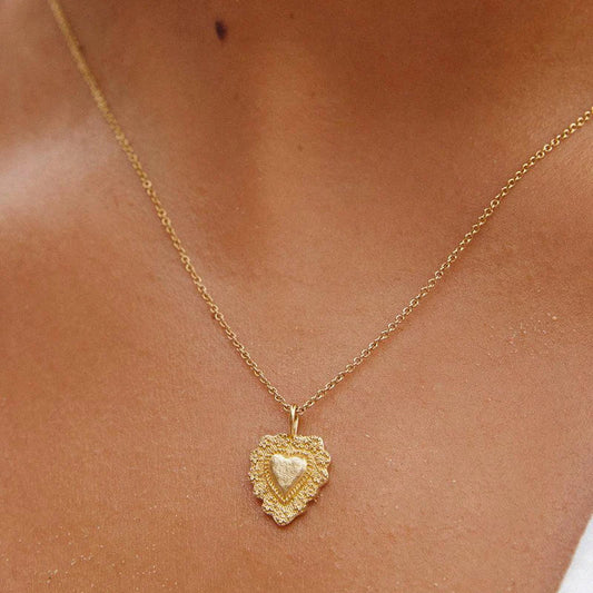 Gold necklace with a heart-shaped pendant on a person's neck