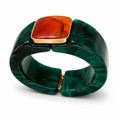 A wide cuff bracelet made of glossy dark green marbled resin, featuring a square raised inset with a warm orange-red stone and a gold-tone border, shown on a clean white background.