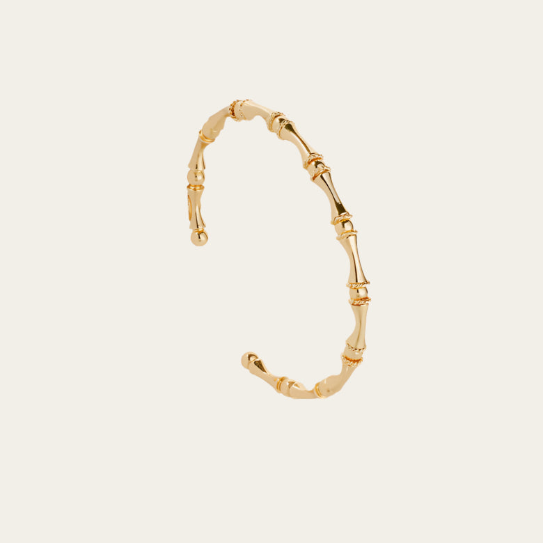 Delicate gold bangle bracelet with twisted bamboo motif, flat lay on neutral background with soft shadows
