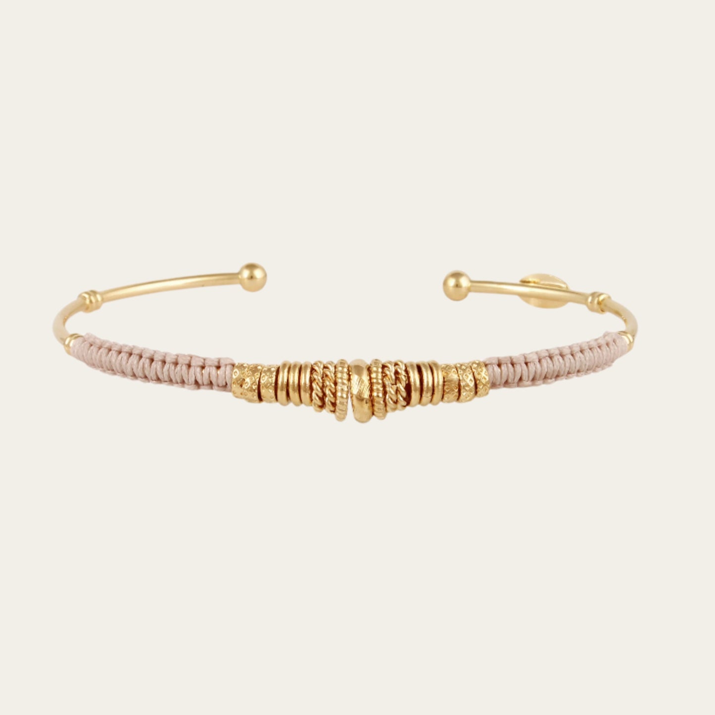 open gold bracelet wrapped in light grey threads and gold rings on neutral background