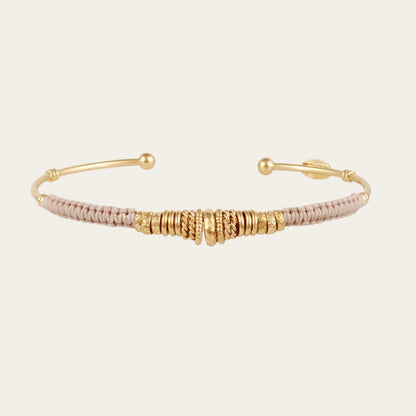 open gold bracelet wrapped in light grey threads and gold rings on neutral background