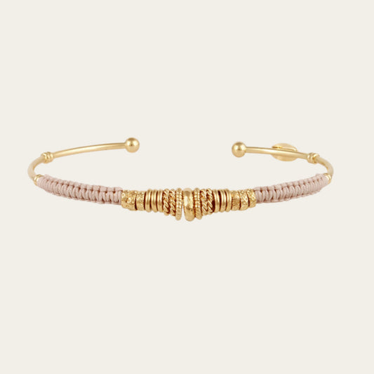 open gold bracelet wrapped in light grey threads and gold rings on neutral background