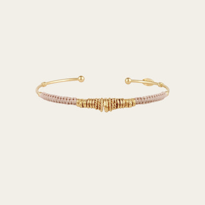gold bangle with coloured threads and gold rings on neutral background