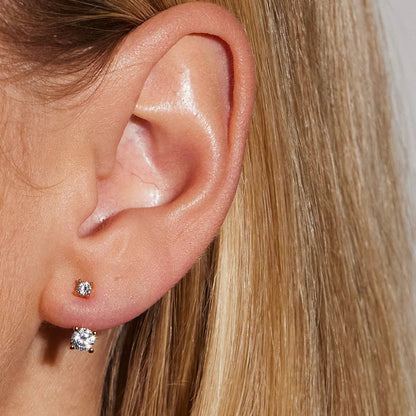 Close-up of a person's ear wearing diamond stud earrings with blonde hair.