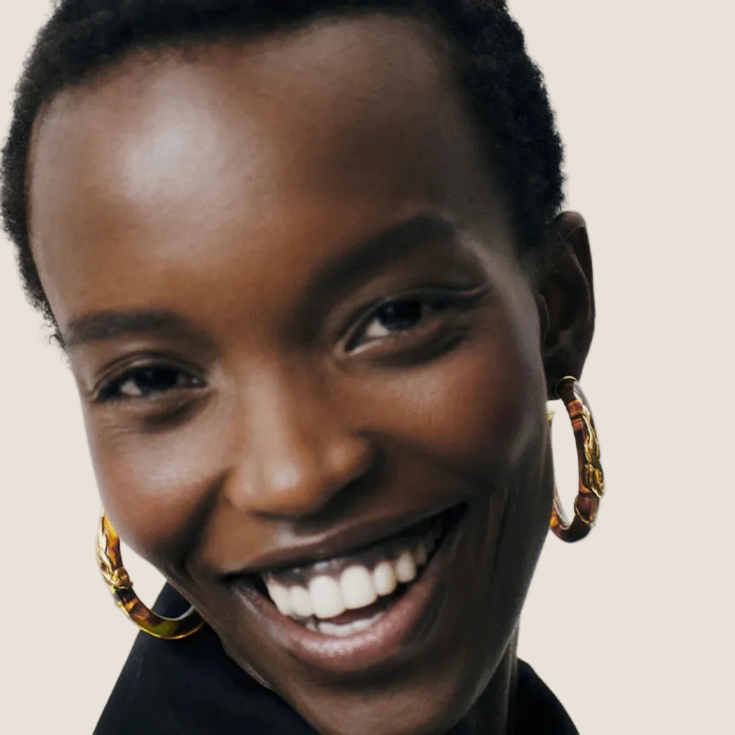 woman wearing brown and gold hoop earrings against a cream background