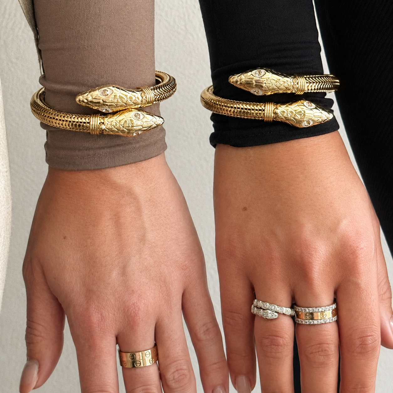 two hands side by side wearing matching gold cobra bangles 