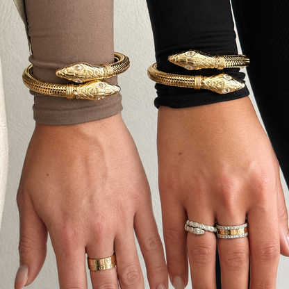 two hands side by side wearing matching gold cobra bangles 