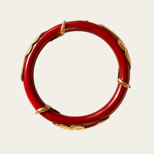 A red circular bangle bracelet decorated with gold-toned serpent, shown against a plain cream background.