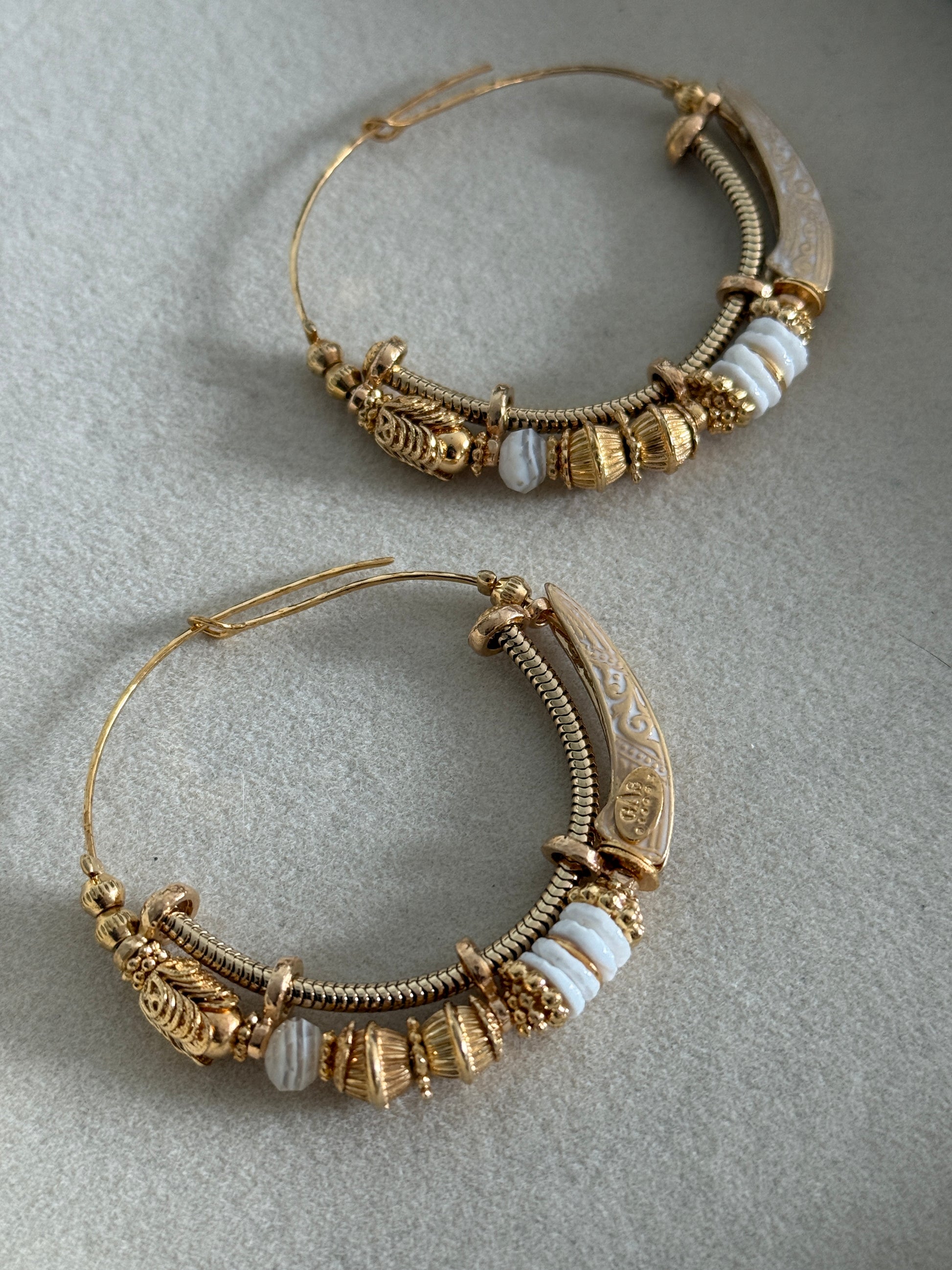 Pair of ornate gold hoop earrings on a gray background