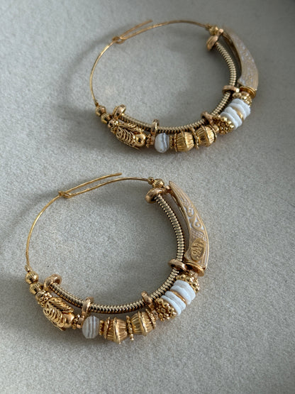 Pair of ornate gold hoop earrings on a gray background