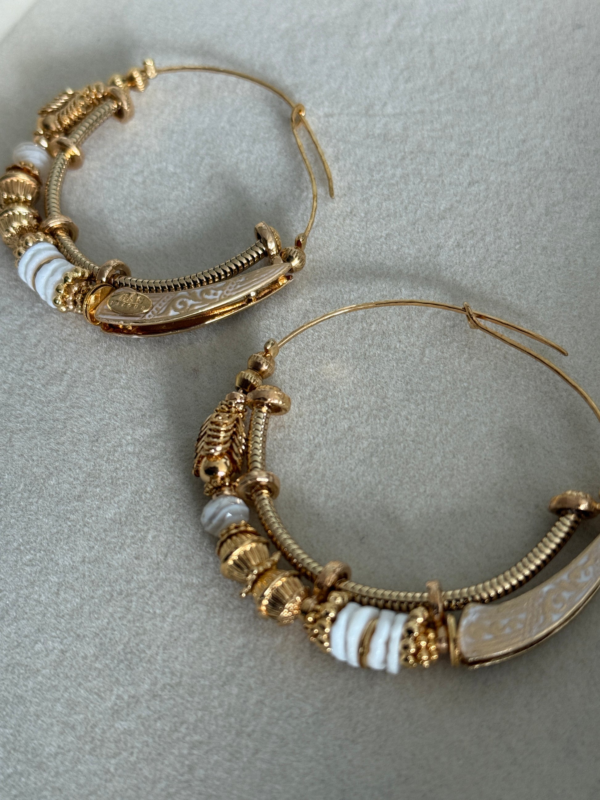 Gold hoop earrings with decorative elements on a light gray background