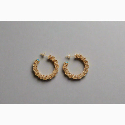 Gold braided hoop earrings with turquoise stones on a grey background 