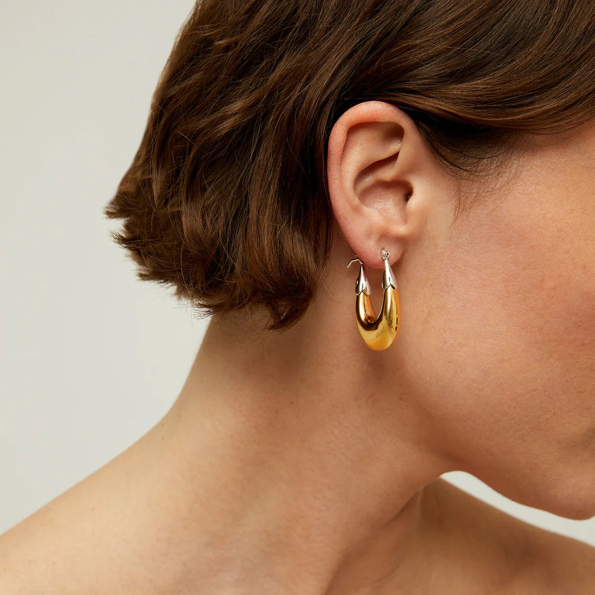 Close-up of a person wearing gold hoop earrings with a neutral background