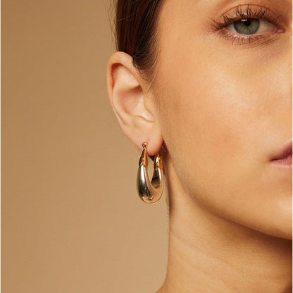 Gold hoop earrings worn by a model against a beige background
