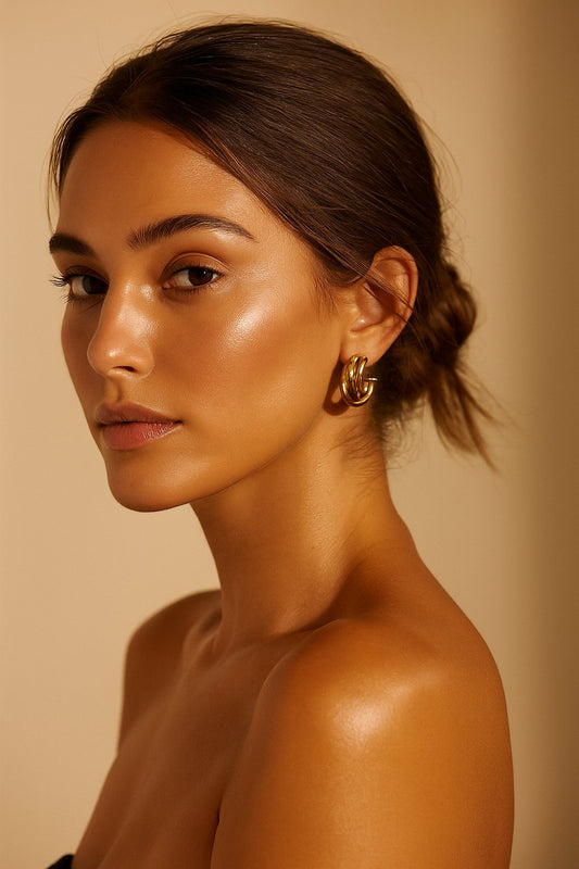 Woman wearing gold earrings against a beige background