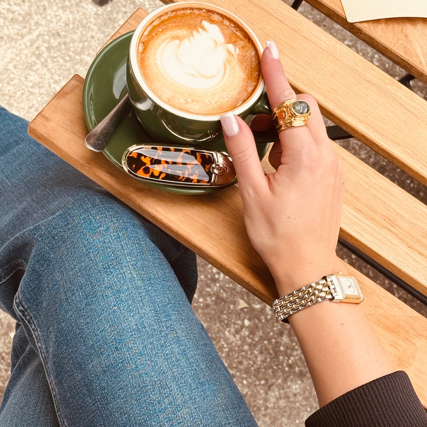 Person holding a cup of coffee on a wooden bench