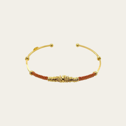 Gold bracelet with brown threads on a beige background
