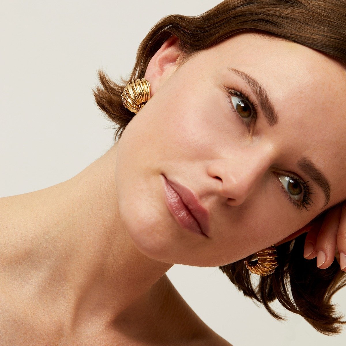 Close-up of a woman wearing gold hoop earrings with a neutral background