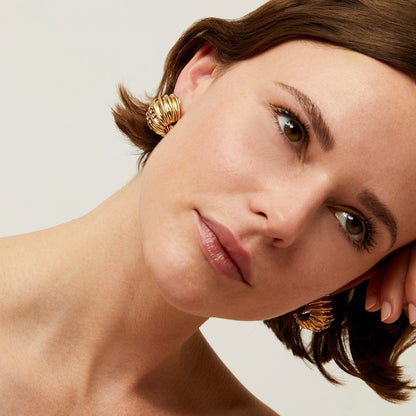 Close-up of a woman wearing gold hoop earrings with a neutral background