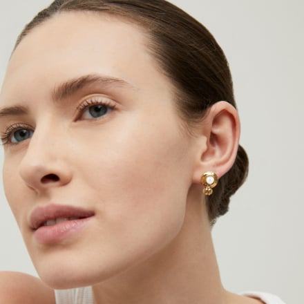 Close-up of a woman wearing gold earrings on a neutral background