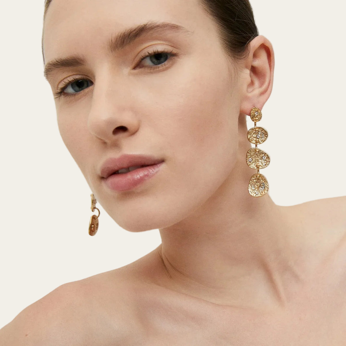 Model wearing Gas Bijoux Éclipse Strass gold-plated drop earrings with hammered linked discs and clear strass detailing, with hair swept back.