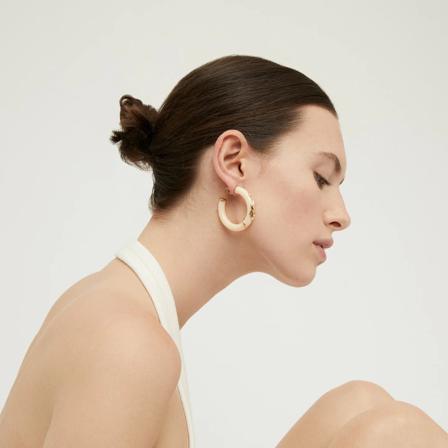 A woman in profile wearing a large gold hoop earring, shown against a clean light gray studio background.