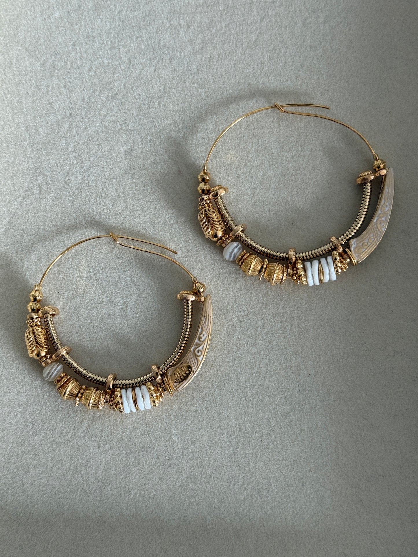 Pair of gold hoop earrings with white beads on a gray background