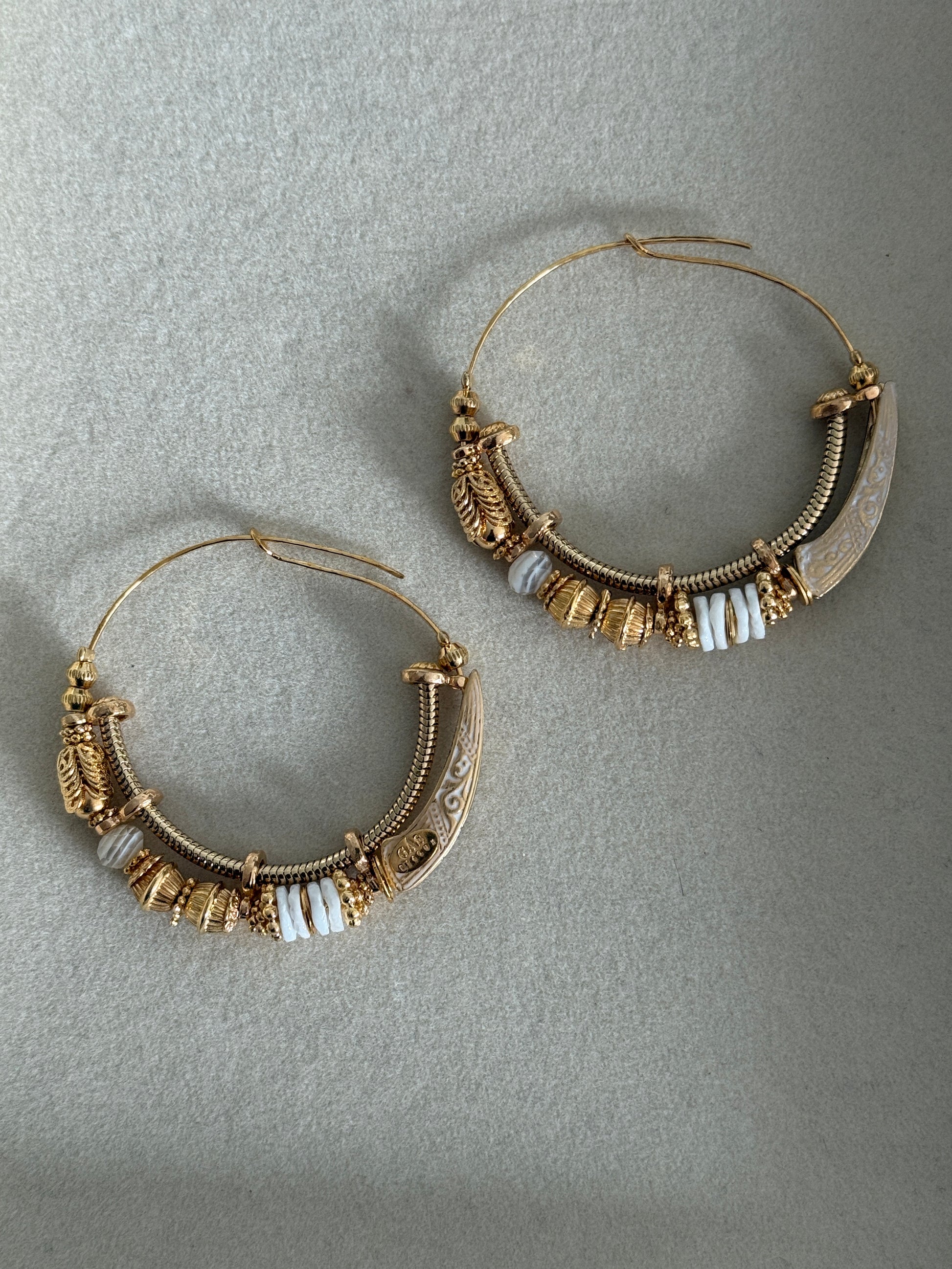 Pair of gold hoop earrings with white beads on a gray background