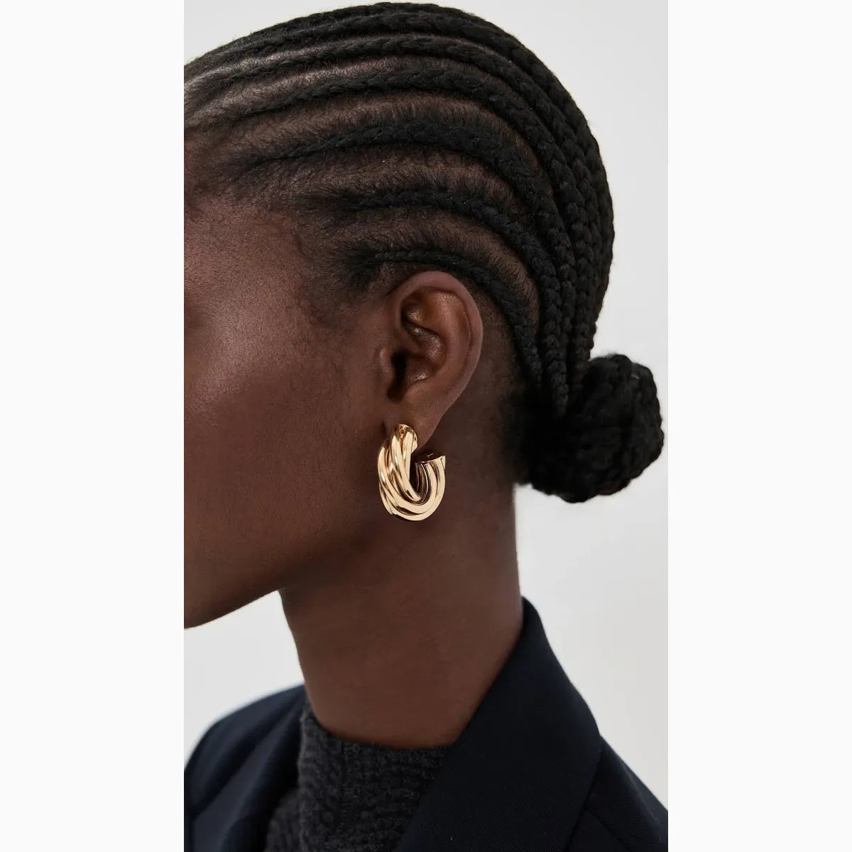 Close-up of an ear wearing a gold hoop earring with braided hair on a neutral background