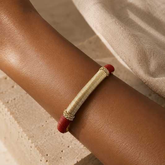 gold bracelet with coloured threads on arm against travertine surface