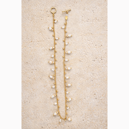 Gold necklacewith pearl-like beads on a beige surface