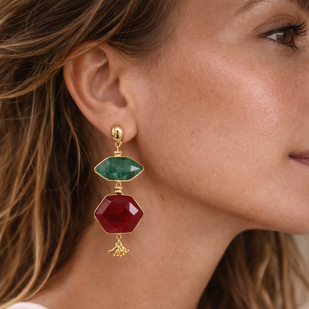 Close-up of a woman wearing gold earrings with green and red gemstones.