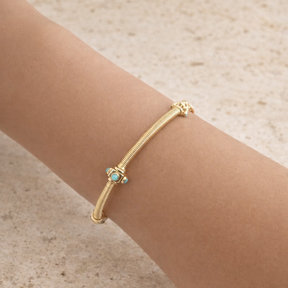 Gold bracelet with a turquoise stone on a wrist against a beige background
