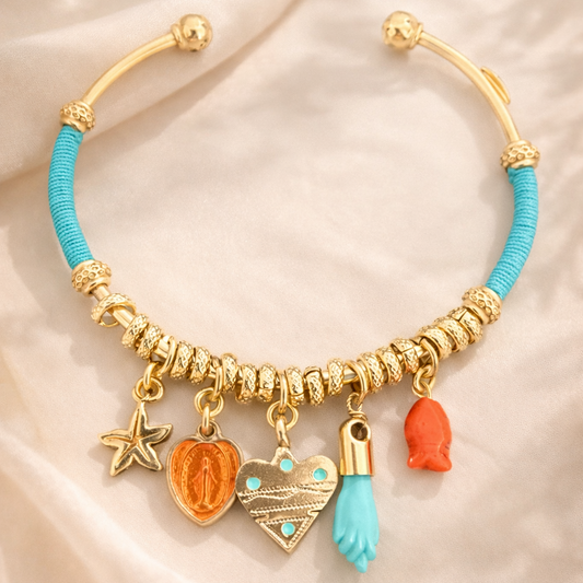 Gold bracelet with turquoise and orange charms on a beige fabric background