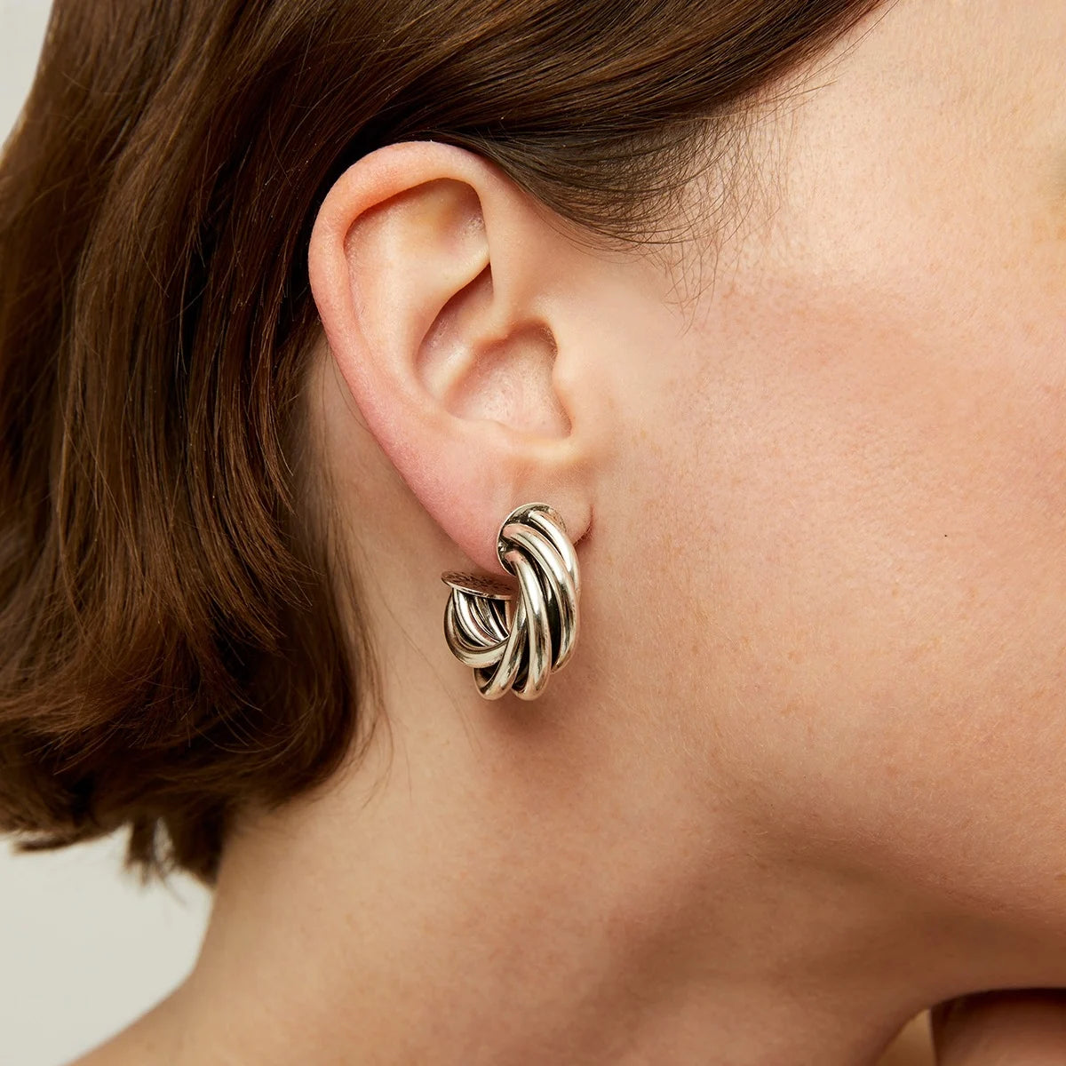 Close-up of an ear wearing a gold hoop earring with a neutral background