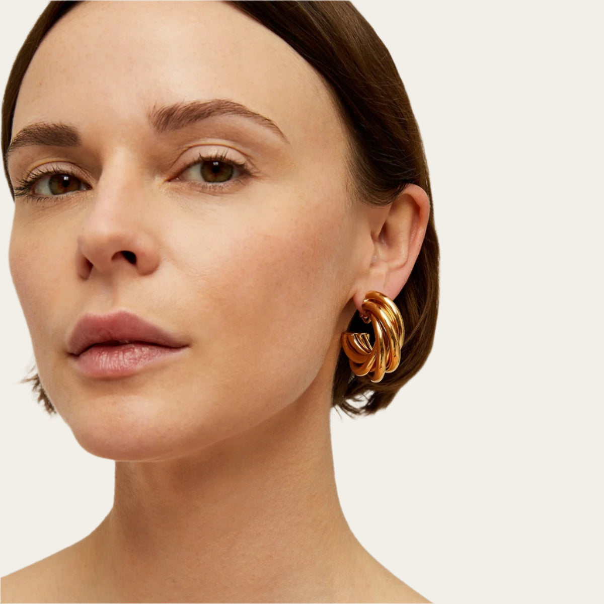 Close-up of a woman wearing gold earrings against a neutral background