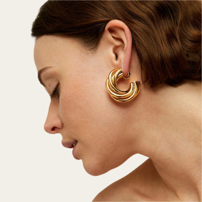 Gold hoop earring worn by a woman on a neutral background