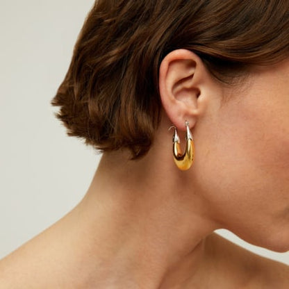 Gold hoop earrings worn by a woman with a neutral background